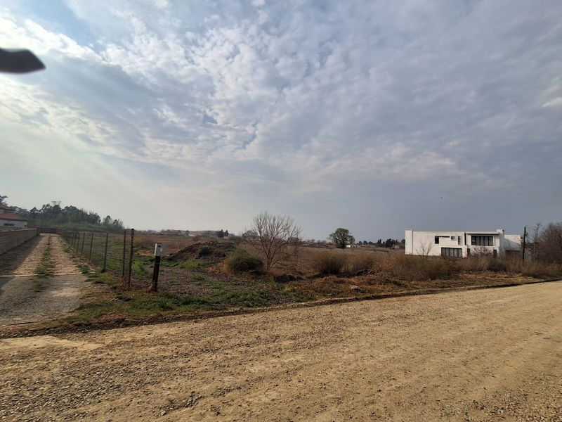 A view of an unimproved residential vacant lot from an unpaved gravel road, featuring wire perimeter fencing and open landscape.