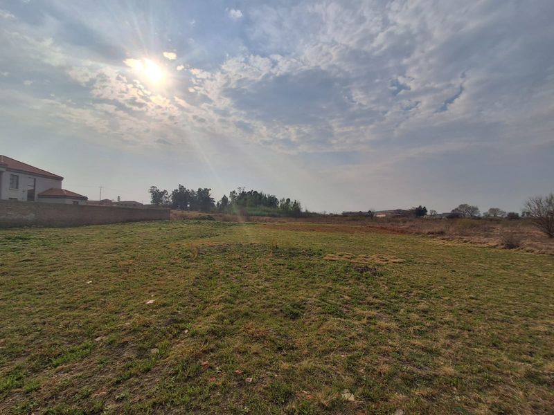 A wide-angle view of a vacant residential plot featuring open grass land and a boundary wall on the side.