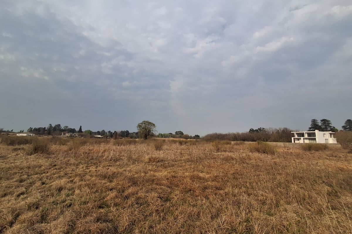 A wide-angle view of a vacant residential plot featuring natural dry grass and surrounding landscape.