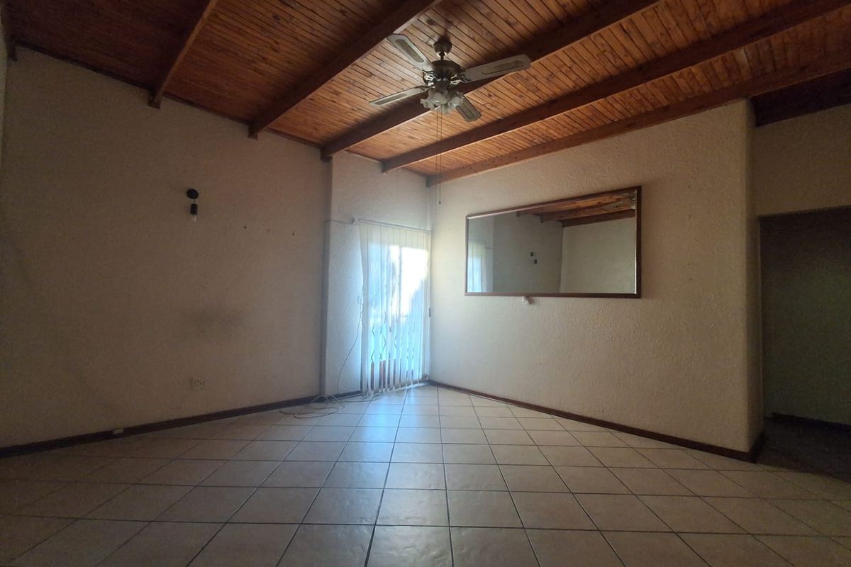 An empty living room featuring a vaulted timber ceiling, ceiling fan, and tiled flooring, with a sliding door providing access to the exterior.