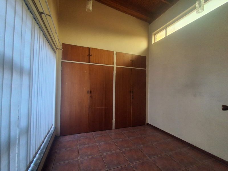 An empty bedroom featuring tiled flooring, built-in wooden cupboards, and an exposed timber ceiling with a clerestory window for natural light.