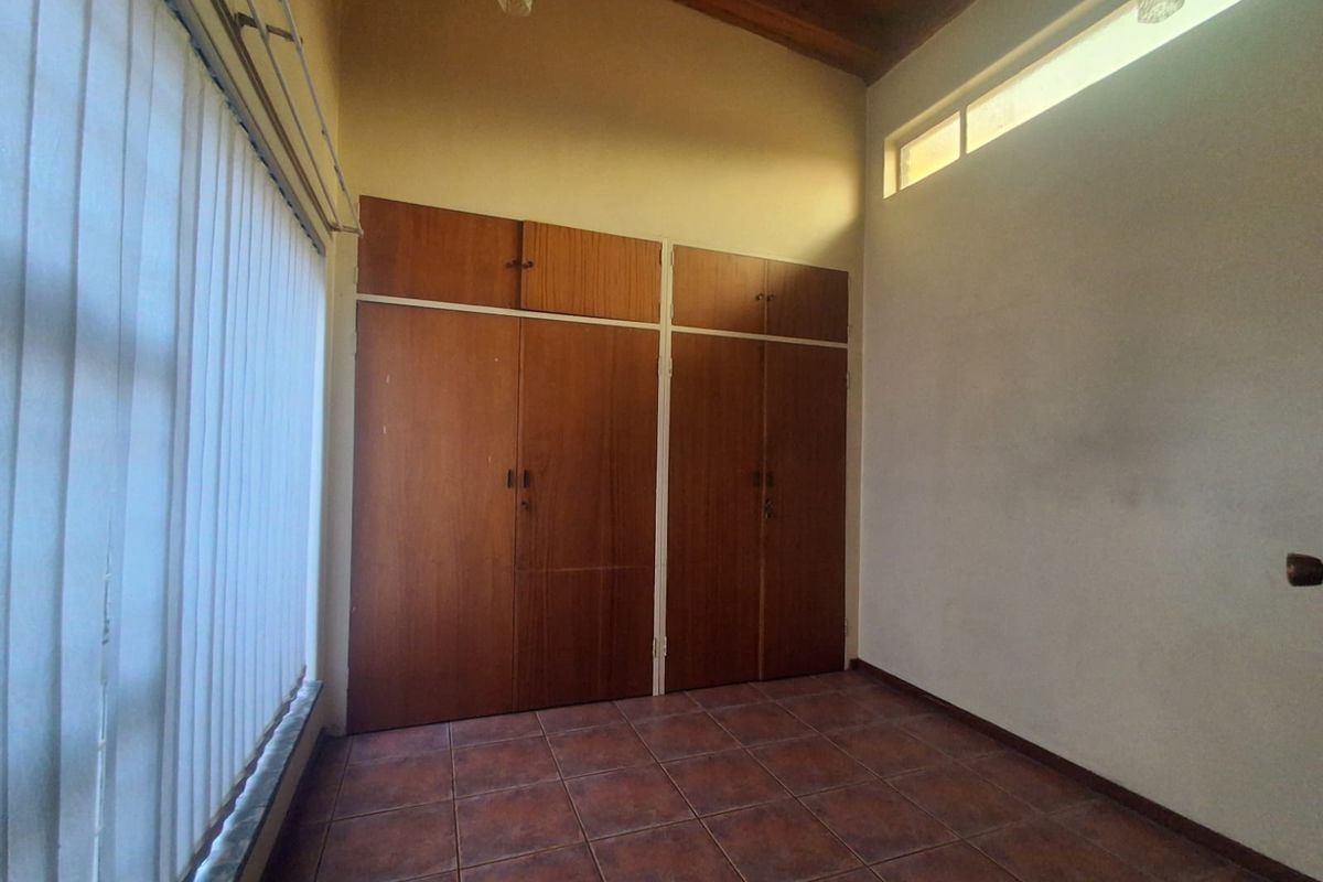 An empty bedroom featuring tiled flooring, built-in wooden cupboards, and an exposed timber ceiling with a clerestory window for natural light.