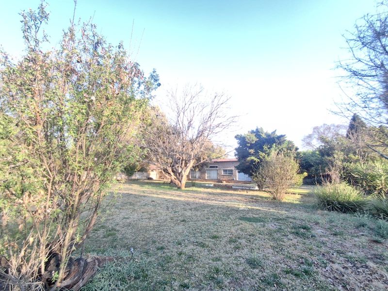 A spacious rear garden featuring mature trees and a view of the property's brick exterior facade.
