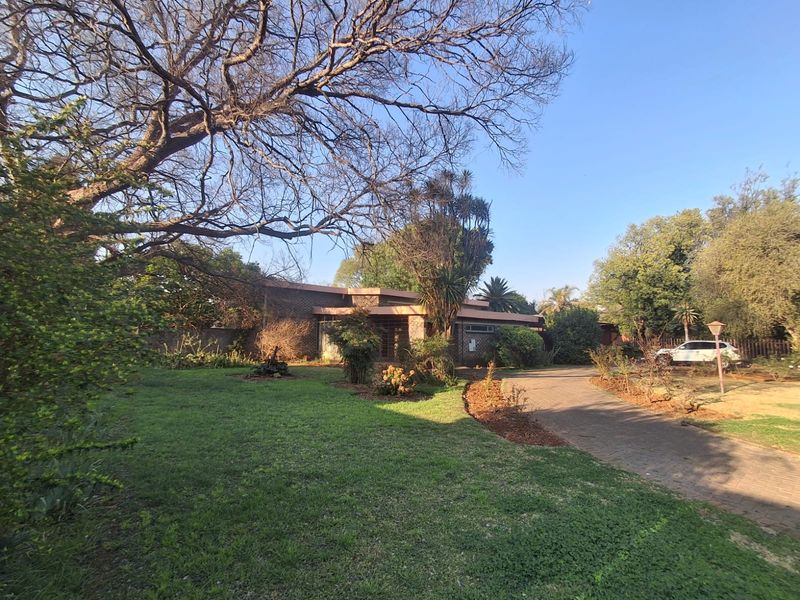 Front view of the property featuring a brick driveway, established garden, and mature trees leading to the main entrance.