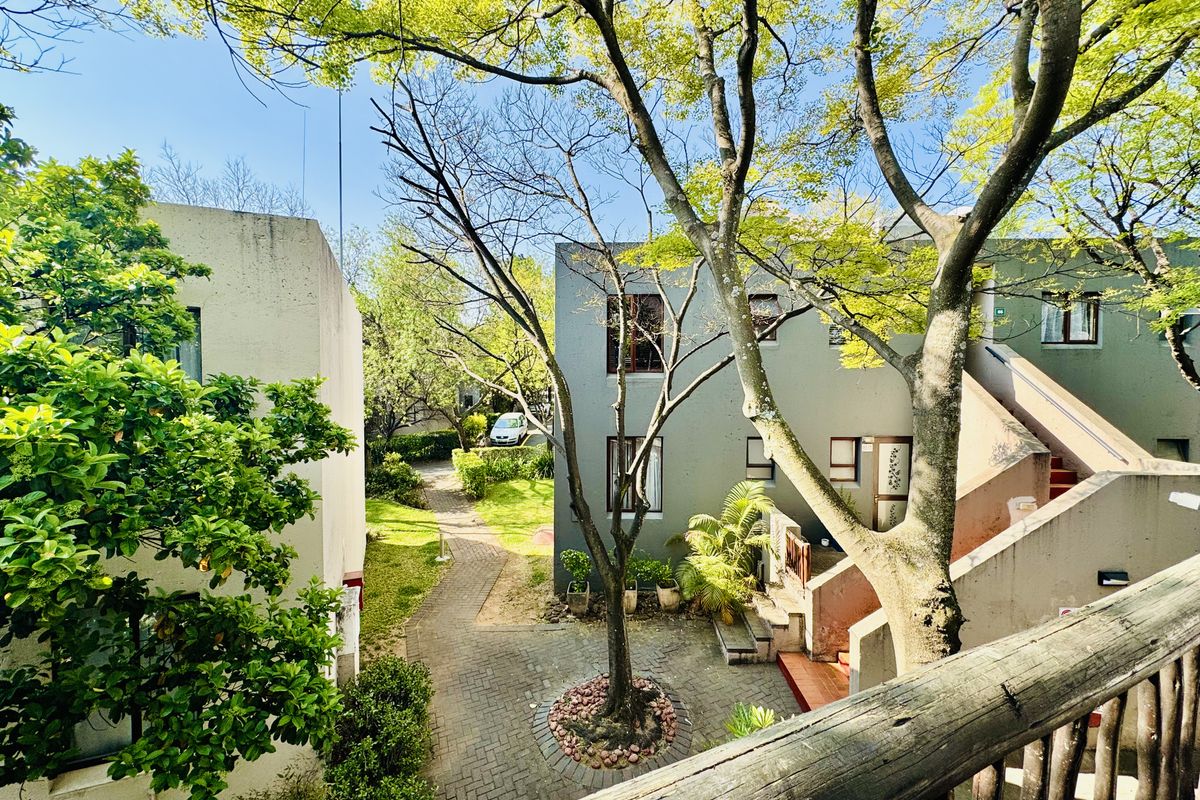 View of a communal courtyard area featuring paved walkways, mature trees, and exterior building facades with access staircases.