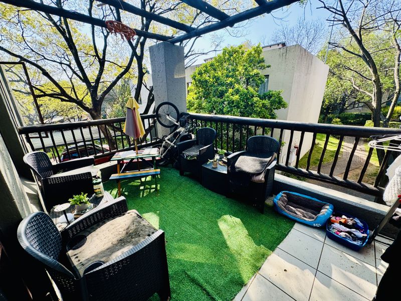 A covered balcony area featuring a timber pergola structure, tiled flooring, and perimeter railing, providing an outdoor space overlooking the surrounding garden area.