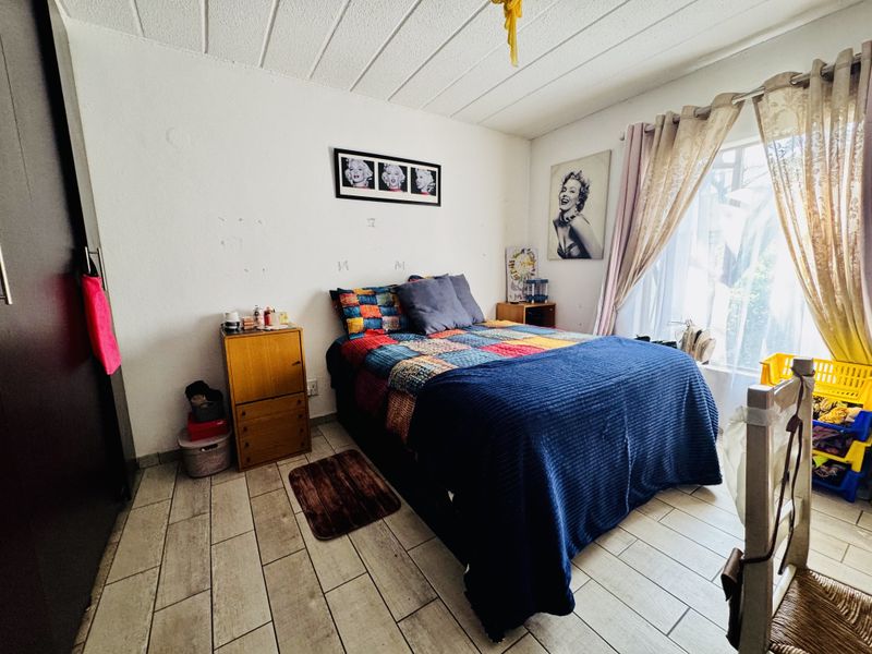 A bedroom featuring tiled flooring, a textured ceiling, and a built-in wardrobe, offering a functional space with potential for cosmetic updates.