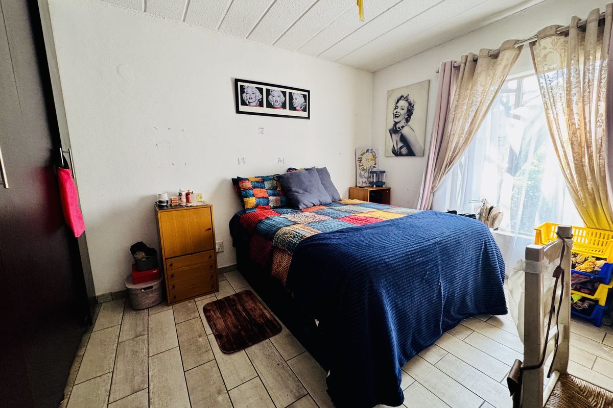 A bedroom featuring tiled flooring, a textured ceiling, and a built-in wardrobe, offering a functional space with potential for cosmetic updates.