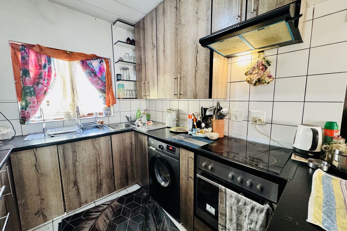A functional kitchen featuring wood-look cabinetry, dark countertops, a built-in oven with extractor fan, and integrated laundry appliance space.