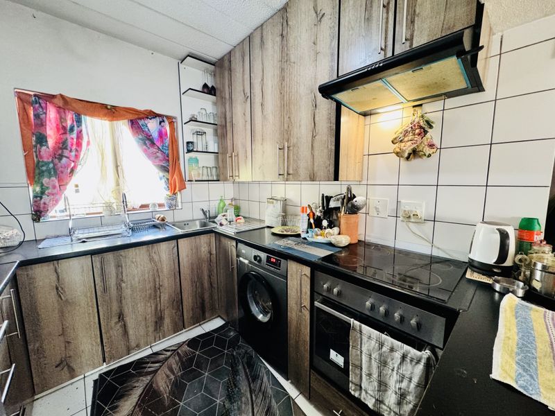 A functional kitchen featuring wood-look cabinetry, dark countertops, a built-in oven with extractor fan, and integrated laundry appliance space.