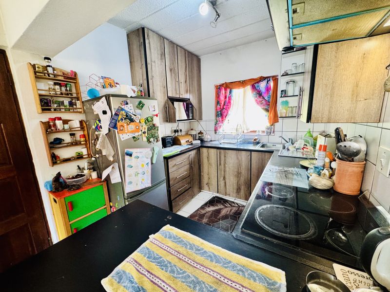 A functional kitchen featuring wood-look cabinetry, dark countertops, an integrated electric hob, and a tiled backsplash, offering a practical layout for daily meal preparation.