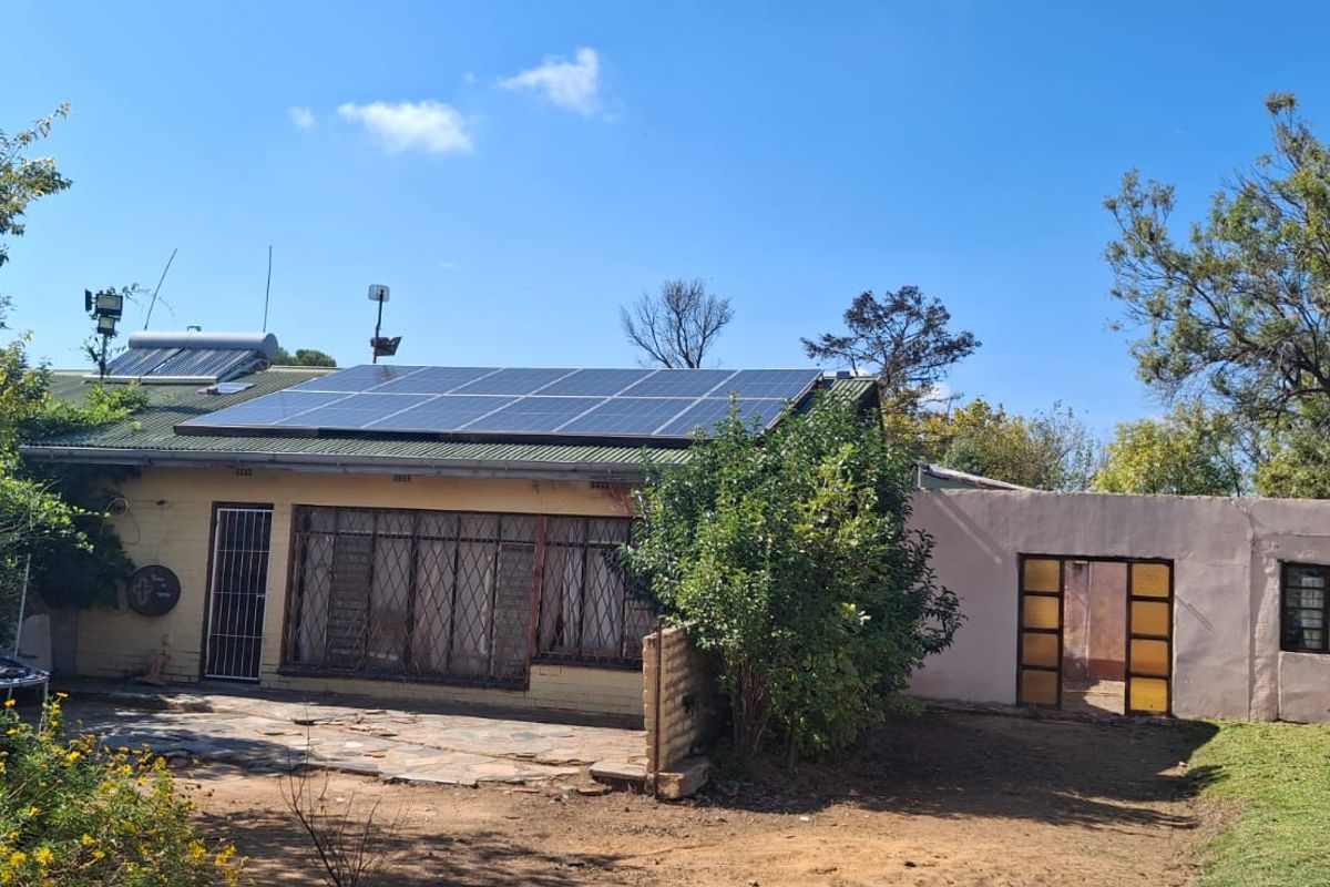Rear view of the farm property featuring a stone patio, security-fitted windows, and a roof-mounted solar power system.