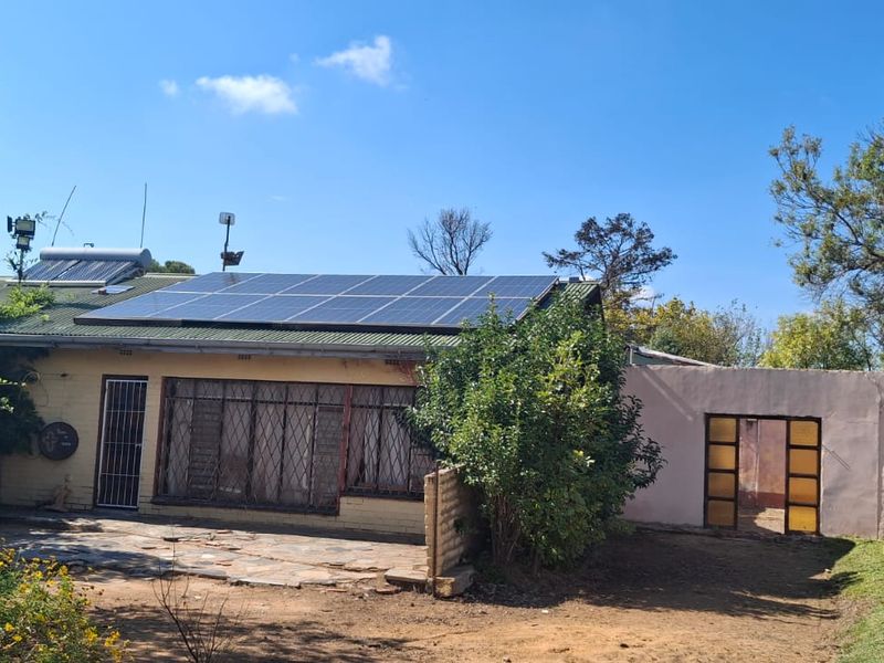 Rear view of the farm property featuring a stone patio, security-fitted windows, and a roof-mounted solar power system.