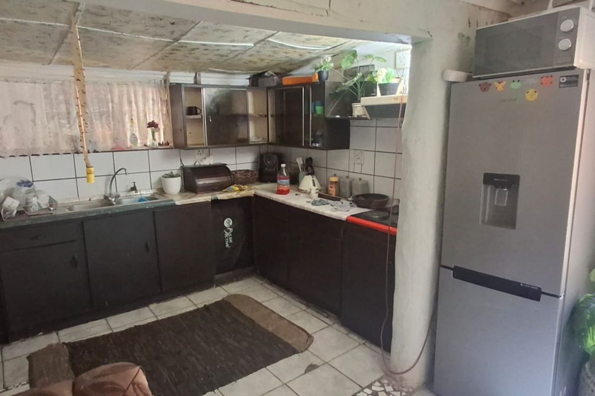 A functional kitchen area featuring dark built-in cabinetry, tiled backsplash, and tiled flooring, requiring cosmetic updates to improve the overall aesthetic and condition.