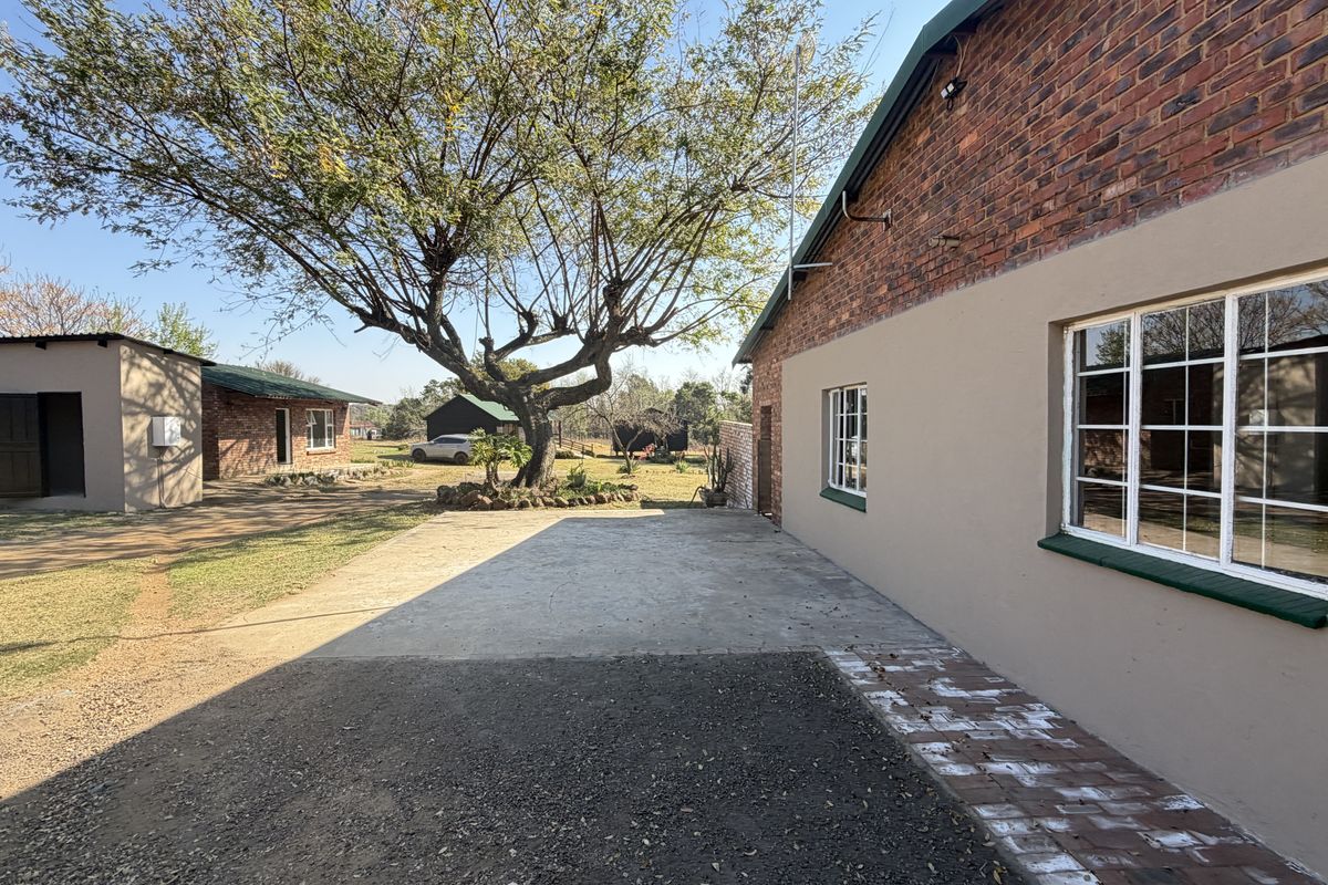 Rear exterior view of the small holding featuring exposed brick walls, concrete driveway, and established trees on the property grounds.