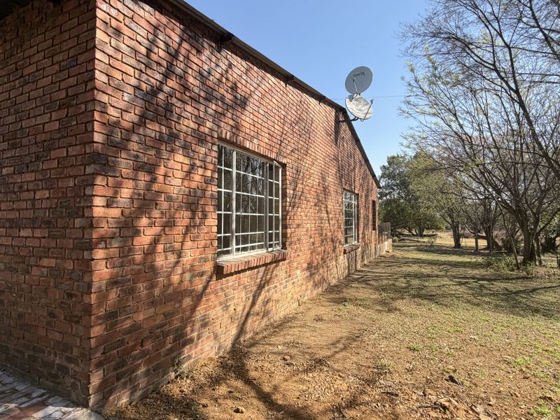 A view of the rear exterior facade featuring face brick walls, steel-framed windows with security bars, and a satellite dish installation.