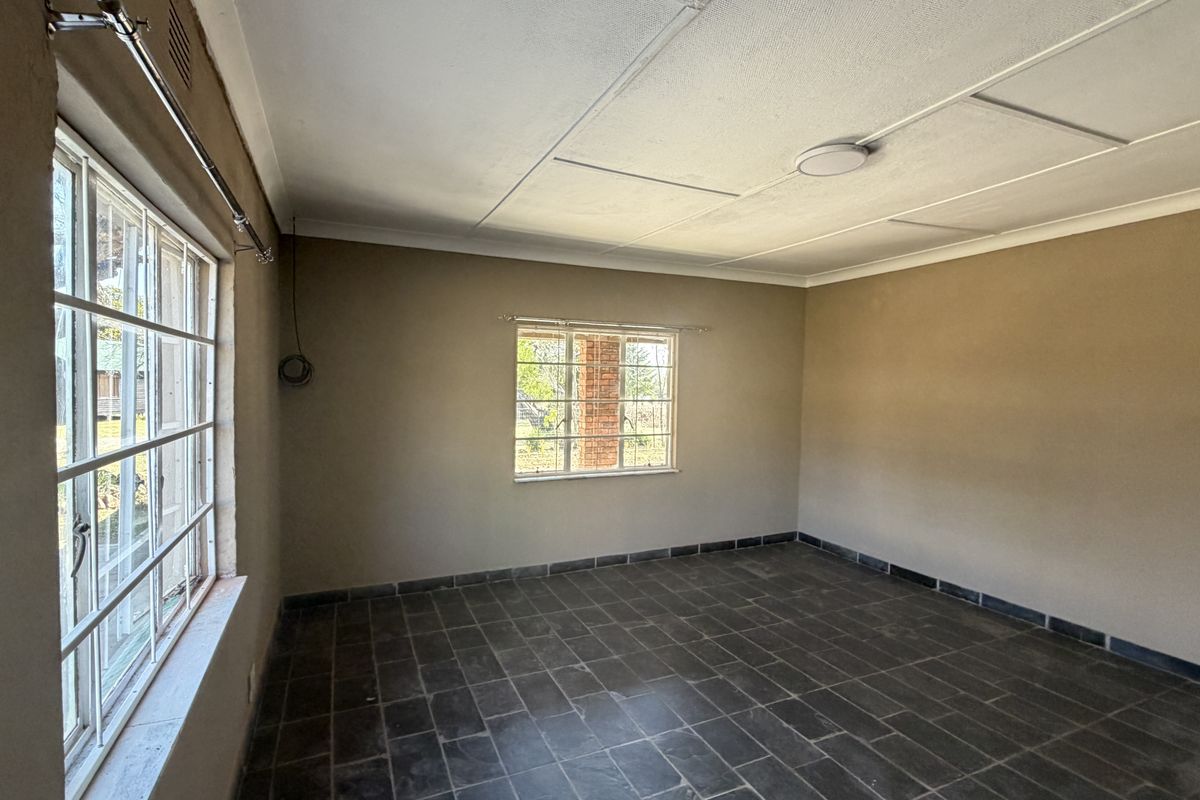 An empty living room featuring dark tiled flooring, steel-framed windows, and exposed ceiling panels, offering a blank canvas for renovation.