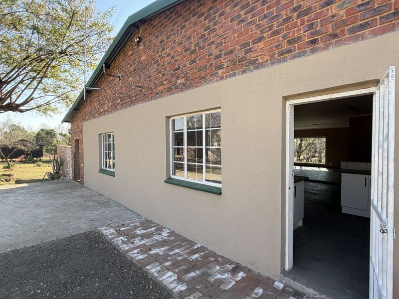 Rear exterior view of the property featuring exposed brick and plastered walls, steel-framed windows, and a paved patio area leading into the interior.