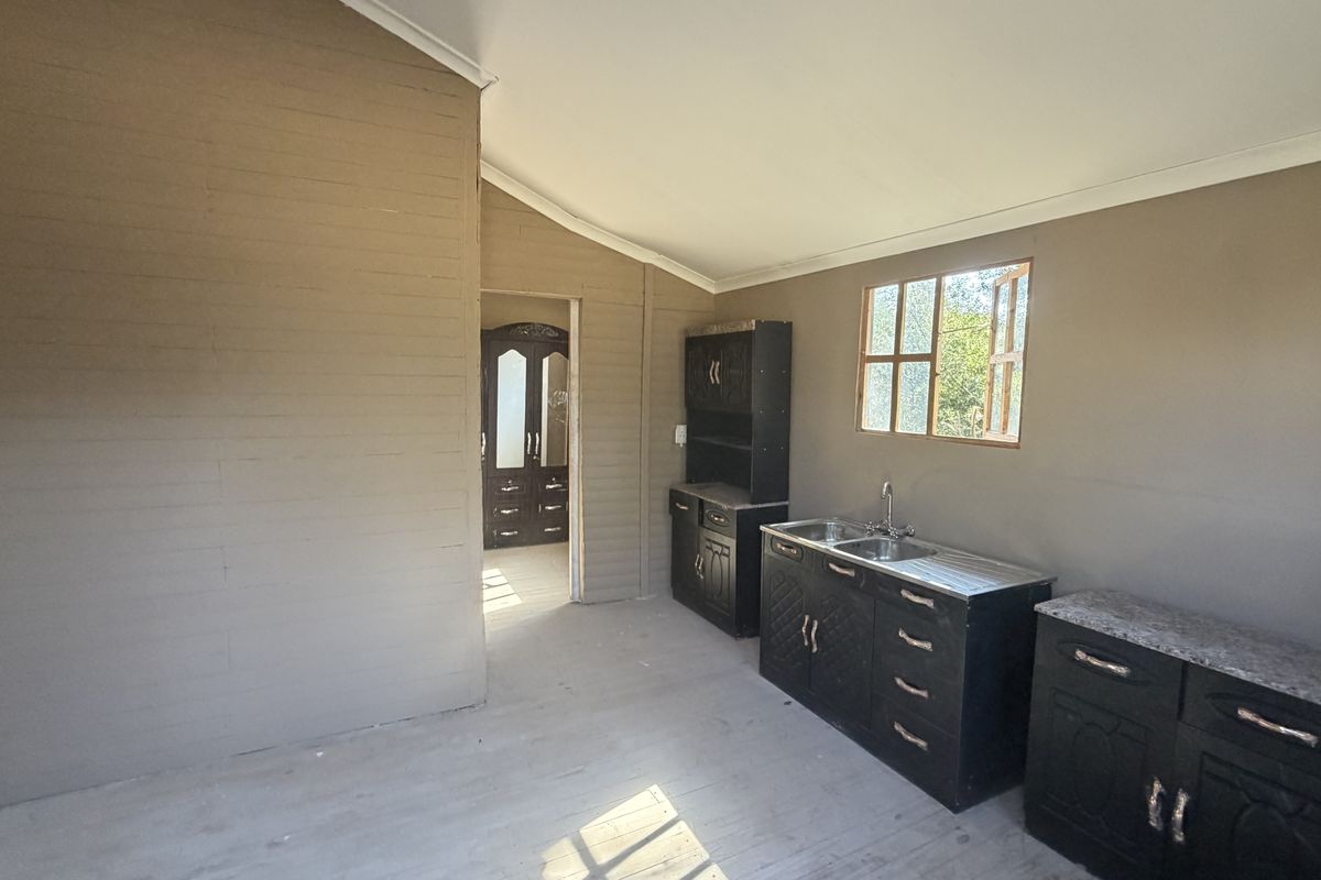 A compact, empty kitchen area featuring dark built-in cabinetry, a double basin sink, and timber-style wall paneling, offering a blank canvas for renovation.