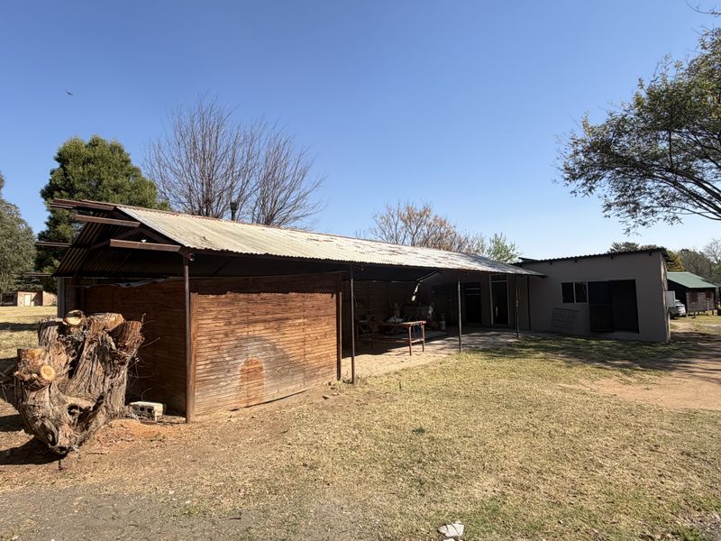 Rear view of a small holding structure featuring a corrugated iron roof, timber cladding, and a covered outdoor workspace area.