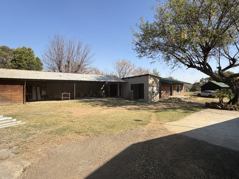 Rear view of the small holding property featuring a large covered outdoor area, brick construction, and expansive garden space.