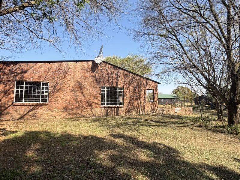 Rear view of a face-brick building featuring steel-framed windows and a satellite dish, set within a spacious garden area.