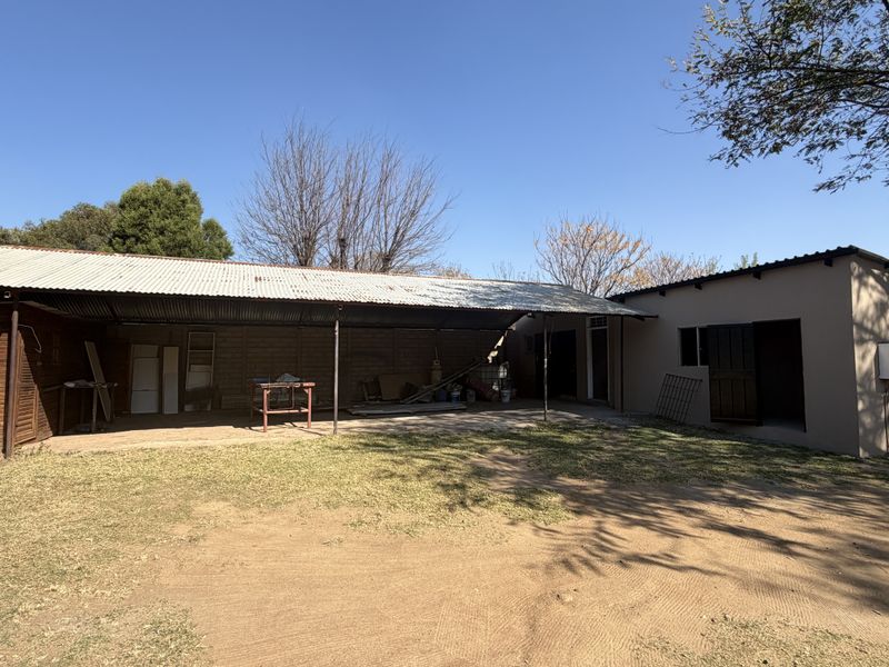 A spacious rear exterior area featuring a large covered patio with corrugated metal roofing, concrete flooring, and timber-clad wall sections.