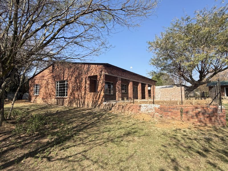 Rear view of a face-brick small holding dwelling featuring a covered patio, security bars on windows, and a brick retaining wall in a garden setting.
