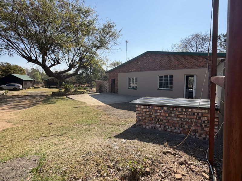 Rear view of the small holding property featuring a brick building, concrete patio area, and an elevated water storage tank.