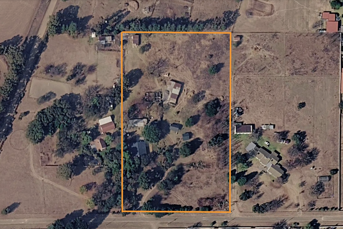 Aerial view of a small holding property featuring multiple outbuildings, established trees, and fenced boundaries within a rural landscape.