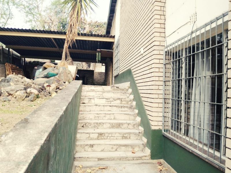 Rear exterior view showing a brick facade, concrete staircase, and a covered carport area with security bars on the windows.