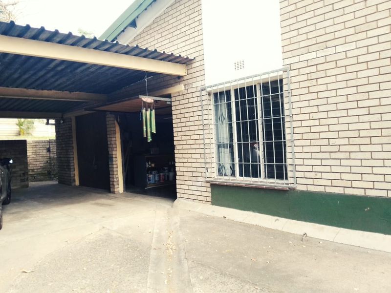 Front exterior view of the house featuring a brick facade, a covered carport area, and security bars on the windows.