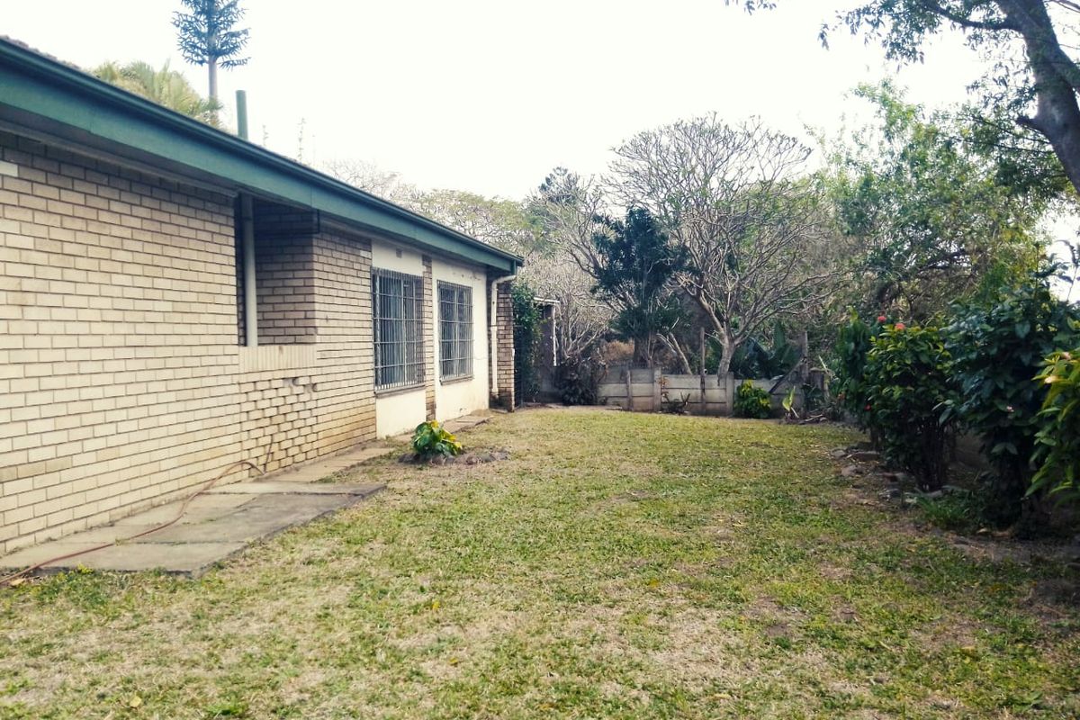 A view of the rear exterior of the house featuring a brick facade, security bars on windows, and a spacious garden area.