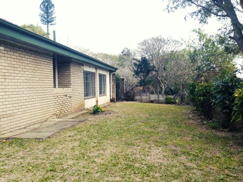 A view of the rear exterior of the house featuring a brick facade, security bars on windows, and a spacious garden area.