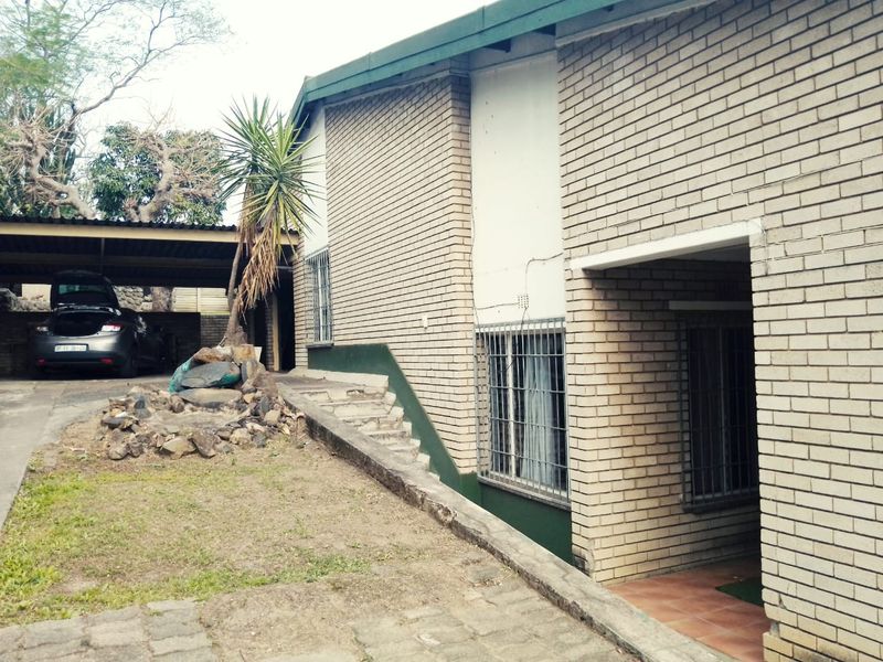 Front exterior view of a brick house featuring a covered carport, security bars on windows, and a paved driveway area.