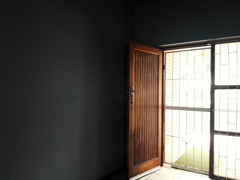 An empty entrance area featuring a solid timber door and a security gate, leading out to an exterior space.