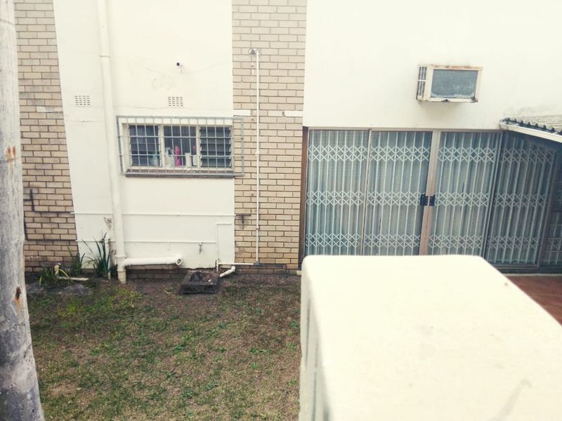 Rear exterior view of the property featuring brick facade, security gates, and window-mounted air conditioning unit overlooking a small garden area.