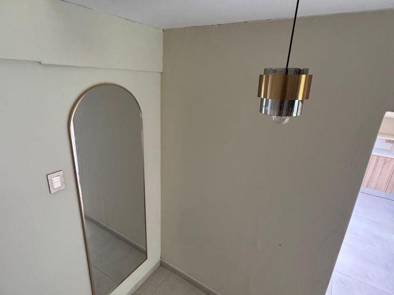 A bright, neutral-toned hallway featuring tiled flooring, a modern pendant light fixture, and a staircase handrail leading to the lower level.