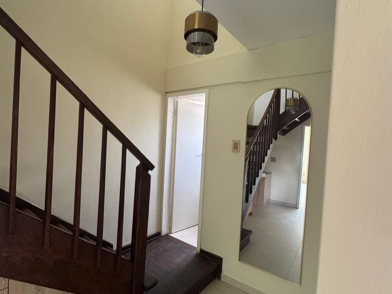 A bright entrance hallway featuring a wooden staircase with a balustrade, tiled flooring, and a modern pendant light fixture.