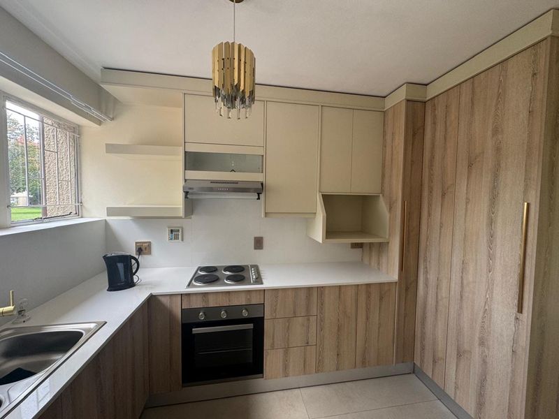 Modern kitchen featuring wood-grain and cream cabinetry, stone countertops, built-in oven, electric hob, extractor fan, and a stainless steel sink.
