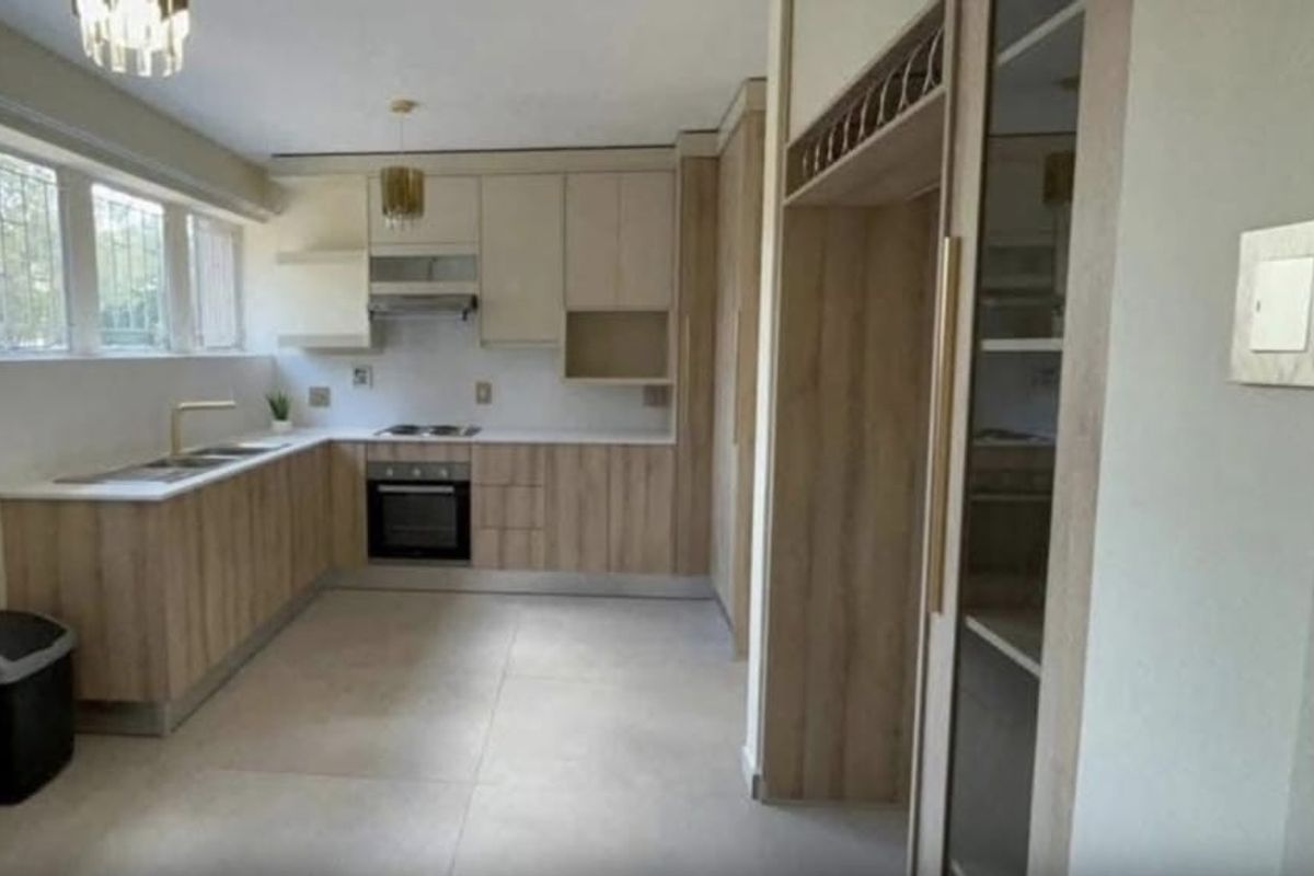 Modern kitchen featuring light wood-tone cabinetry, integrated appliances, stone-look tiled flooring, and ample counter space with a functional layout.