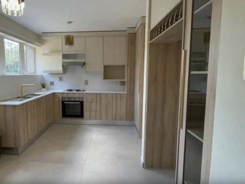 Modern kitchen featuring light wood-tone cabinetry, integrated appliances, stone-look tiled flooring, and ample counter space with a functional layout.