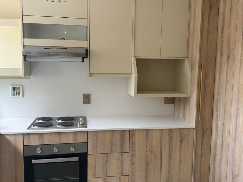 Modern kitchen featuring wood-grain and cream cabinetry, integrated electric hob, oven, extractor fan, and stone countertops with neutral floor tiles.