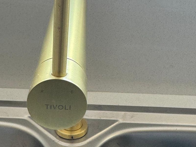 Close-up view of a modern brass kitchen mixer tap installed over a stainless steel sink.
