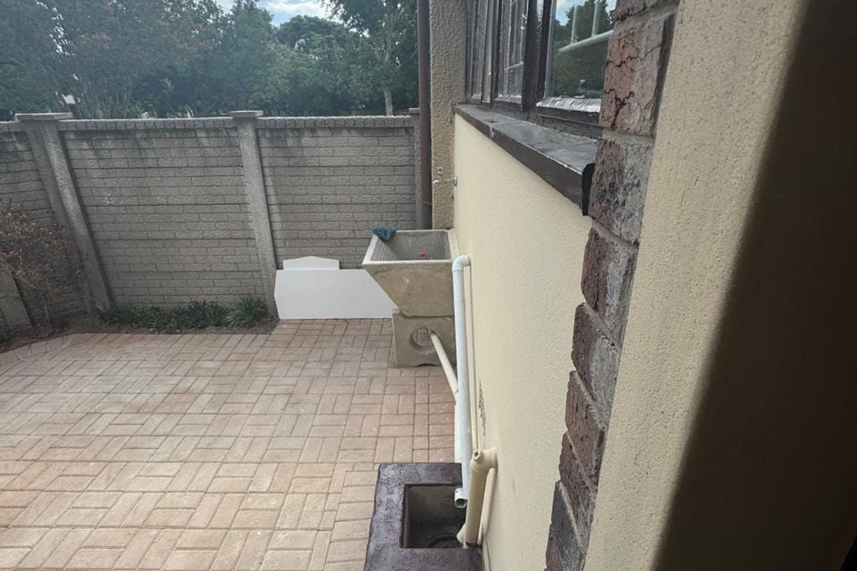 A paved rear courtyard area featuring a brick boundary wall and an external utility sink with exposed plumbing.