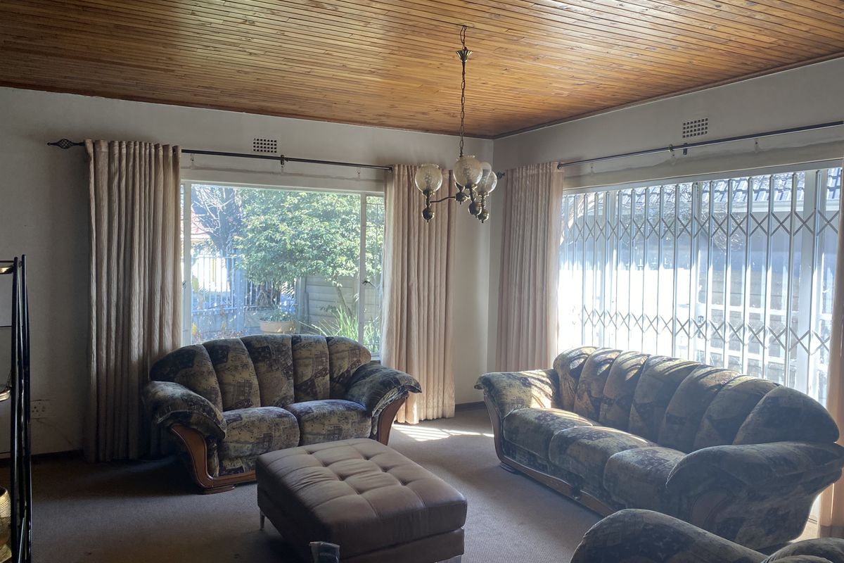 A living room featuring a timber tongue and groove ceiling, large windows with security gates, and carpeted flooring.
