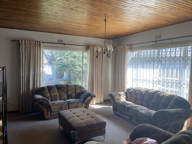 A living room featuring a timber tongue and groove ceiling, large windows with security gates, and carpeted flooring.