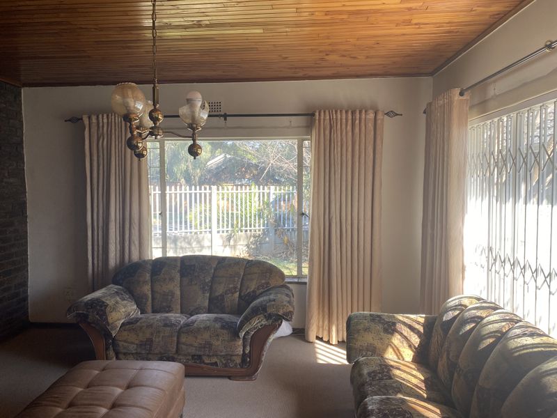 Living room featuring a timber tongue and groove ceiling, brick feature wall, and large windows with security gates.