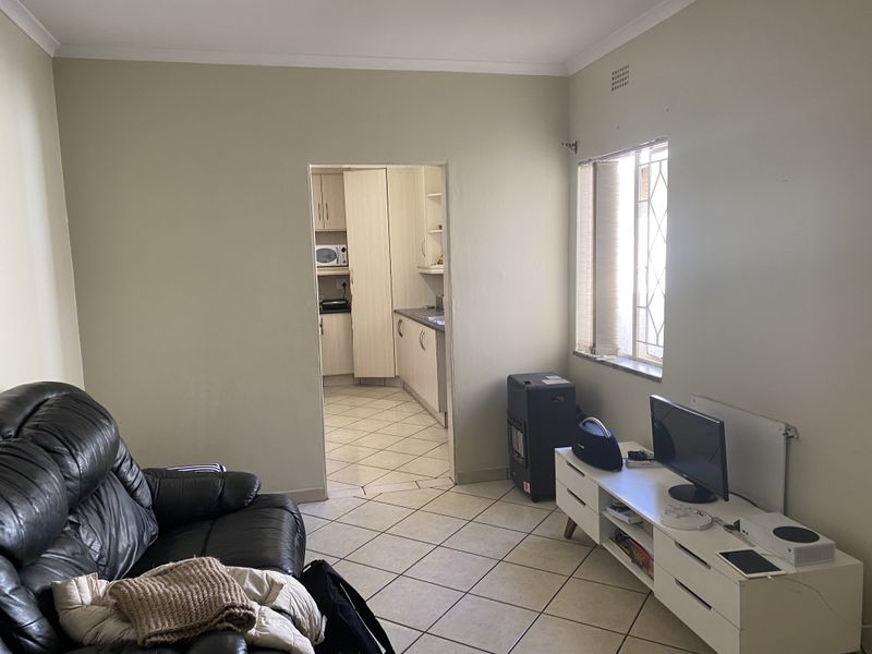 A living room with tiled flooring and a coved ceiling, featuring a direct doorway leading into the adjacent kitchen area.