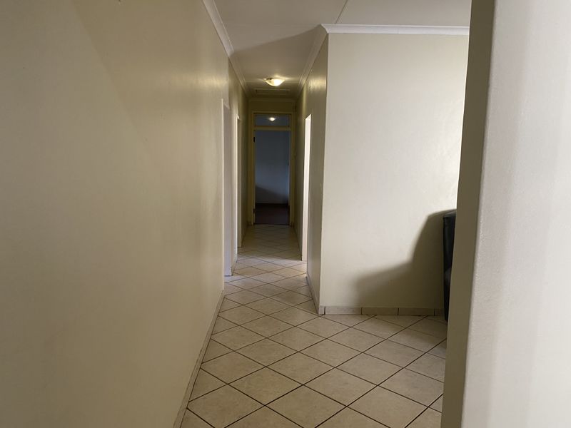 A neutral-toned hallway featuring tiled flooring and simple cornice detailing, providing access to multiple rooms within the home.